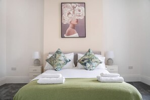 Ein Hotelzimmer mit Bett, Kissen, einer grünen Decke, einem Bild an der Wand und Nachttischlampen.