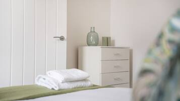 A bedroom with a bed, a green towel, a dresser, and a vase on top.
