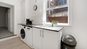 A modern kitchen with a washing machine, a sink, and a window with a view of a brick building. - 4BR South Shields Stay Sleeps 8 by Stay With Us (South Shields)