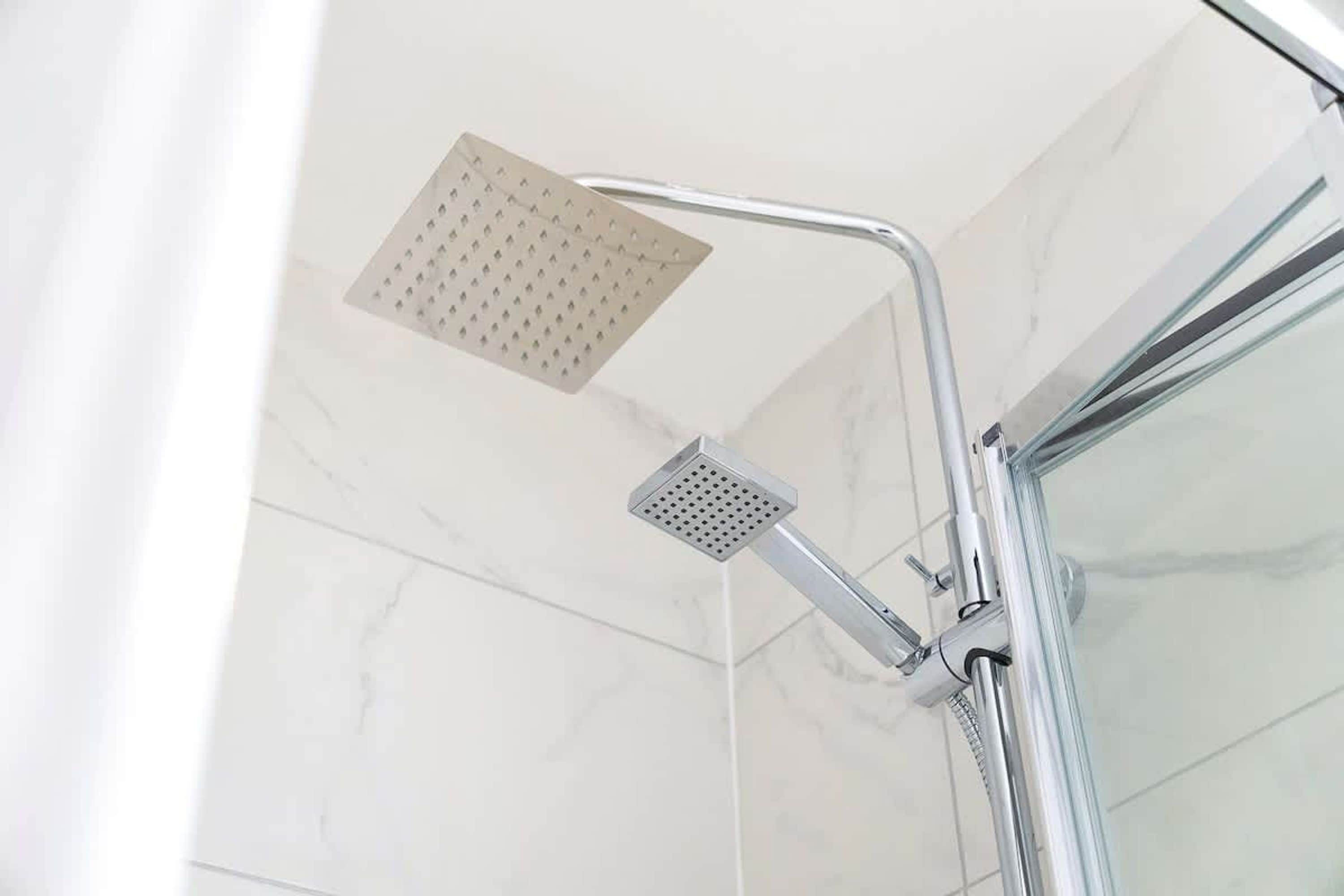 A shower with a square showerhead and a handheld shower attachment.