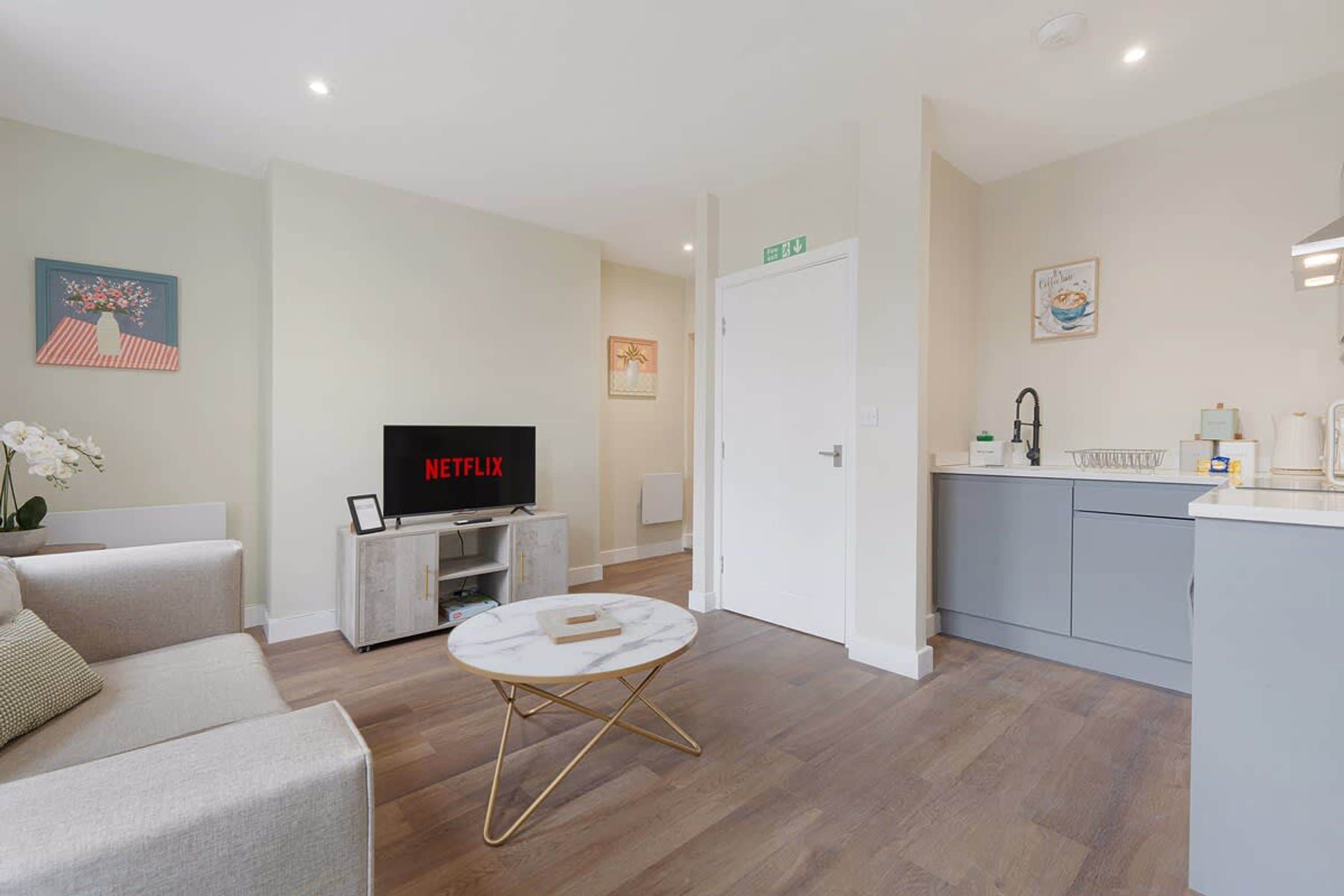 A modern living room with a flat-screen TV, a sofa, a coffee table, and a kitchen area with a sink and countertop.