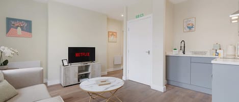 A modern living room with a flat-screen TV, a sofa, a coffee table, and a kitchen area with a sink and countertop.