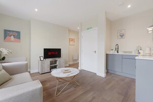 Una sala moderna con televisor de pantalla plana, un sofá, una mesita de centro y una cocina con pileta y mostrador.