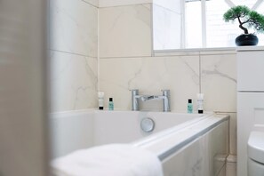 A modern bathroom with a bathtub, a window, and a potted plant. - Stylish 1-bed Stay in the Heart of Barnard Castle (Barnard Castle)