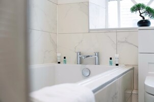 Un baño moderno con bañera, ventana y una planta en maceta.