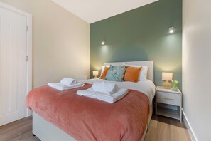 A hotel room with a bed, a nightstand, a lamp, and a door. - Stylish 1-bed Stay in the Heart of Barnard Castle (Barnard Castle)