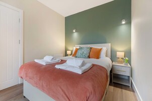 Una habitación de hotel con una cama, una mesita de noche, una lámpara y una puerta.