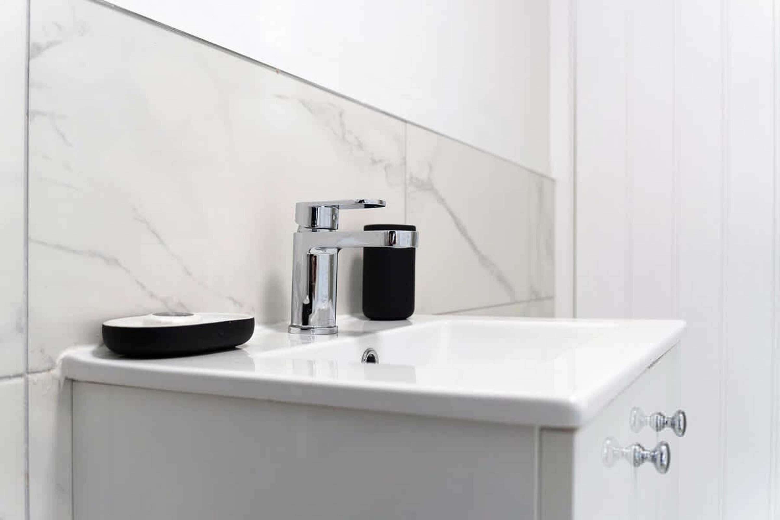Un baño con lavamanos de mármol blanco, grifo cromado y dispensador de jabón negro.