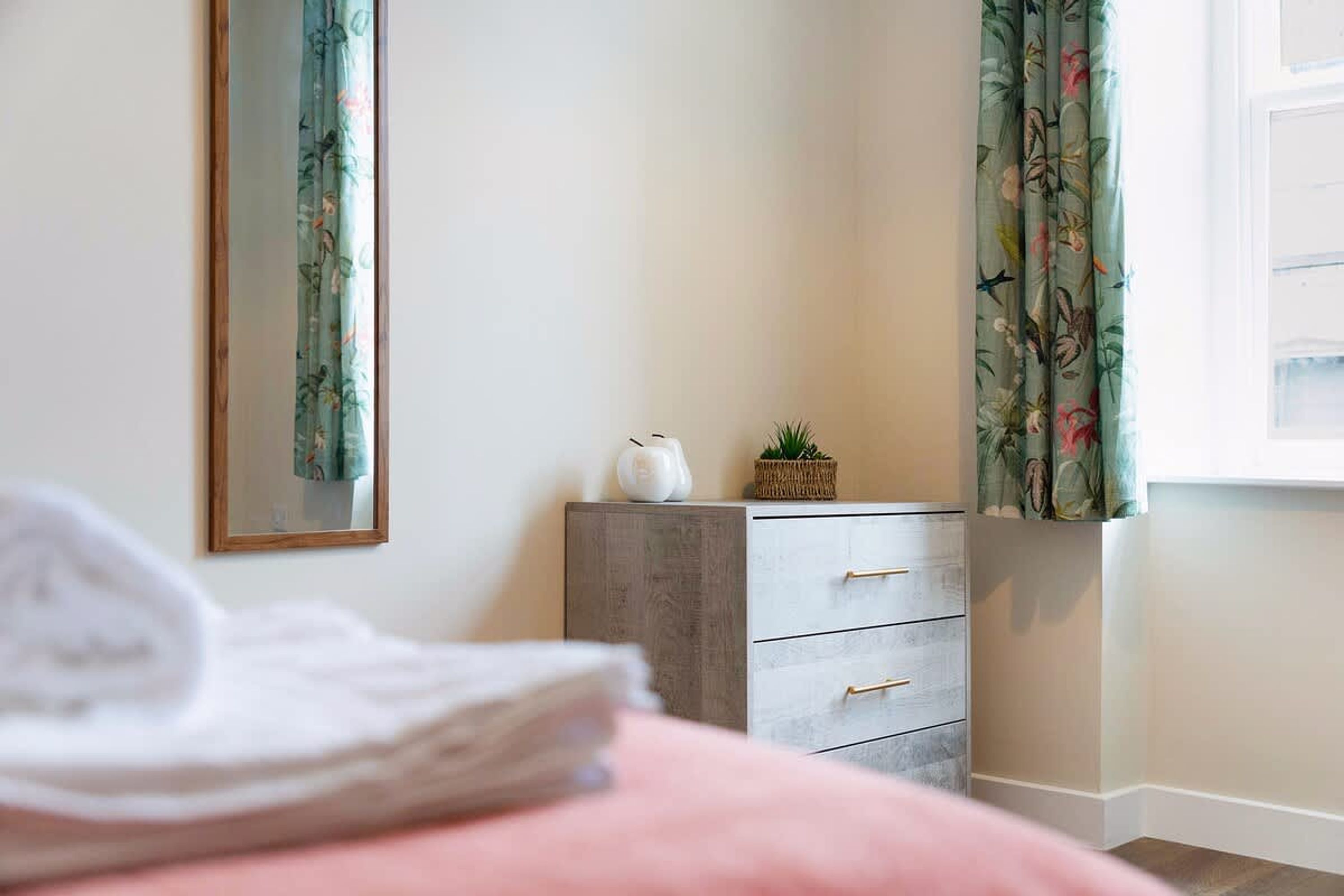 A bedroom with a bed, a dresser, a mirror, and a window with curtains.