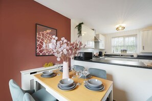 Uma cozinha moderna com armários brancos, uma mesa de jantar posta para quatro pessoas, com pratos, copos e um vaso de flores.