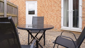 A patio area with a round table and chairs, a door, and a window with a view. - Teesside 3BR Family Retreat Sleeps 5 by Stay With Us (Stockton-on-Tees)