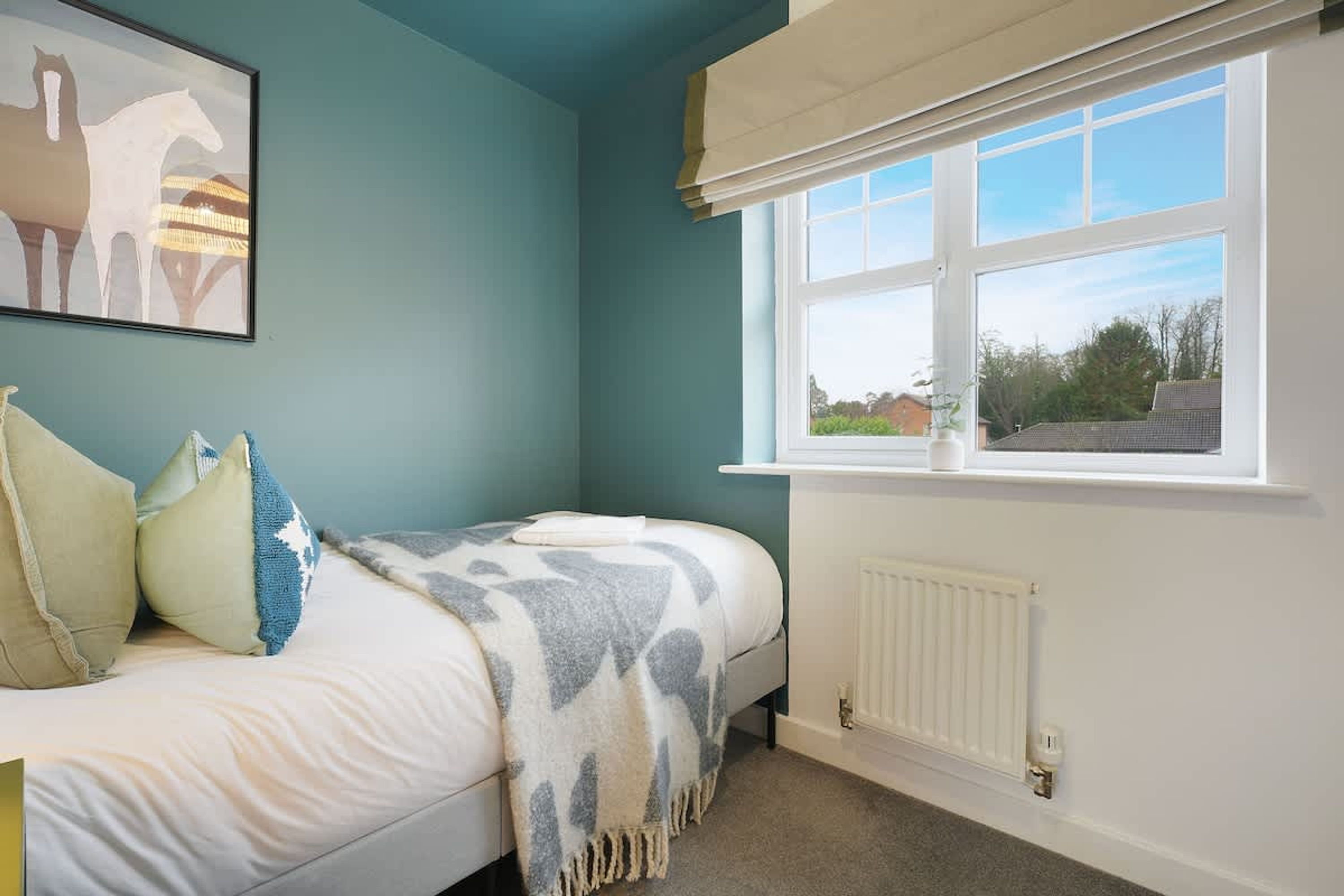 Een slaapkamer met een bed, kussens, een raam met uitzicht en een radiator.