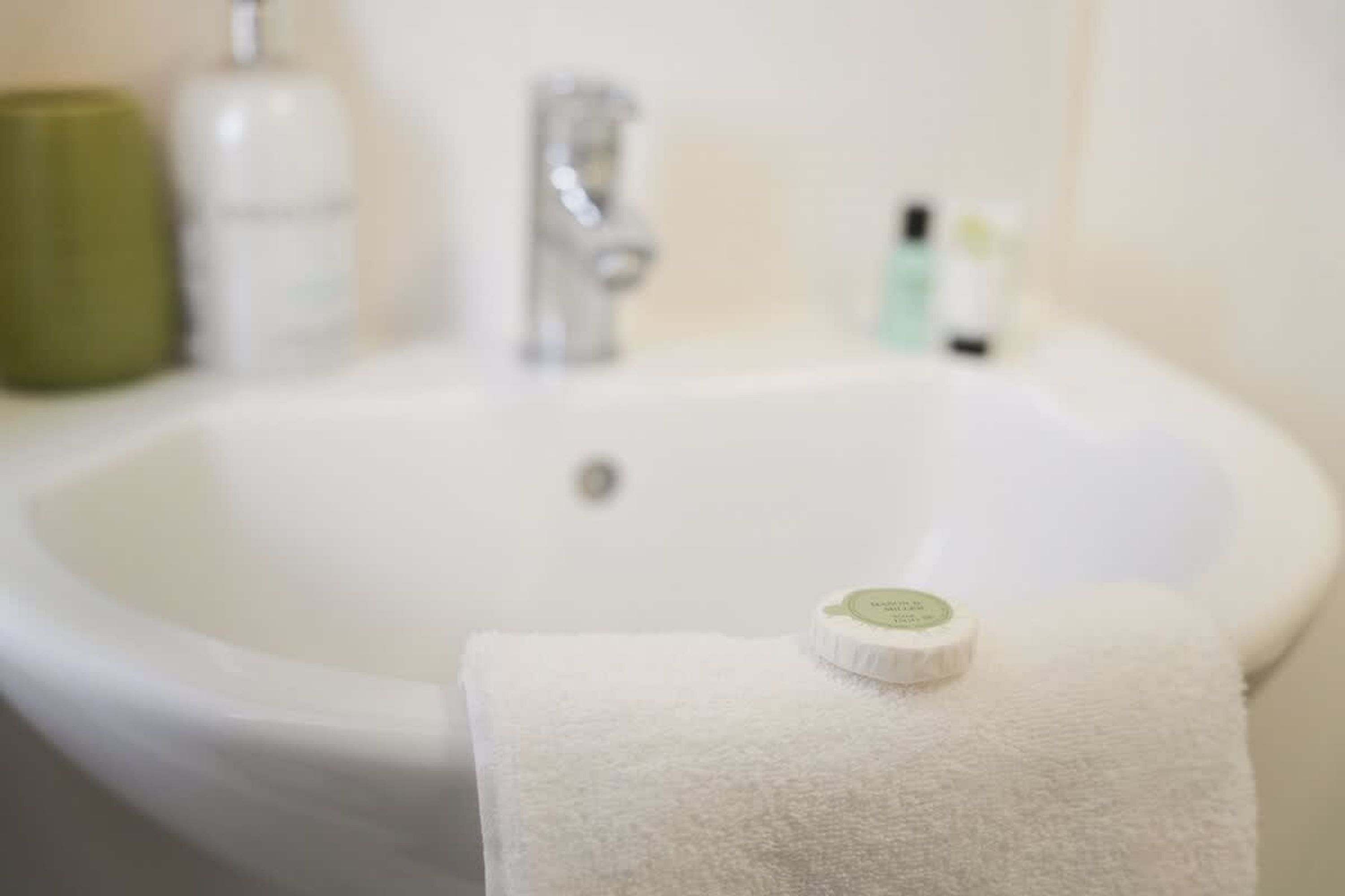 A bathroom with a white sink, a green bottle, and a white towel.