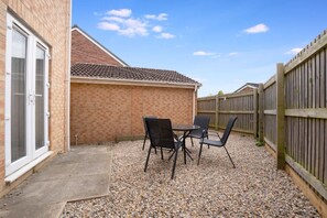 A patio area with a table and chairs, a brick wall, and a wooden fence. - Teesside 3BR Family Retreat Sleeps 5 by Stay With Us (Stockton-on-Tees)