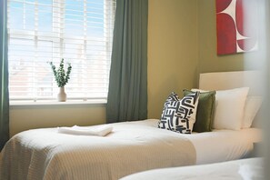 A hotel room with a bed, a window with blinds, a potted plant, and a painting on the wall. - Teesside 3BR Family Retreat Sleeps 5 by Stay With Us (Stockton-on-Tees)
