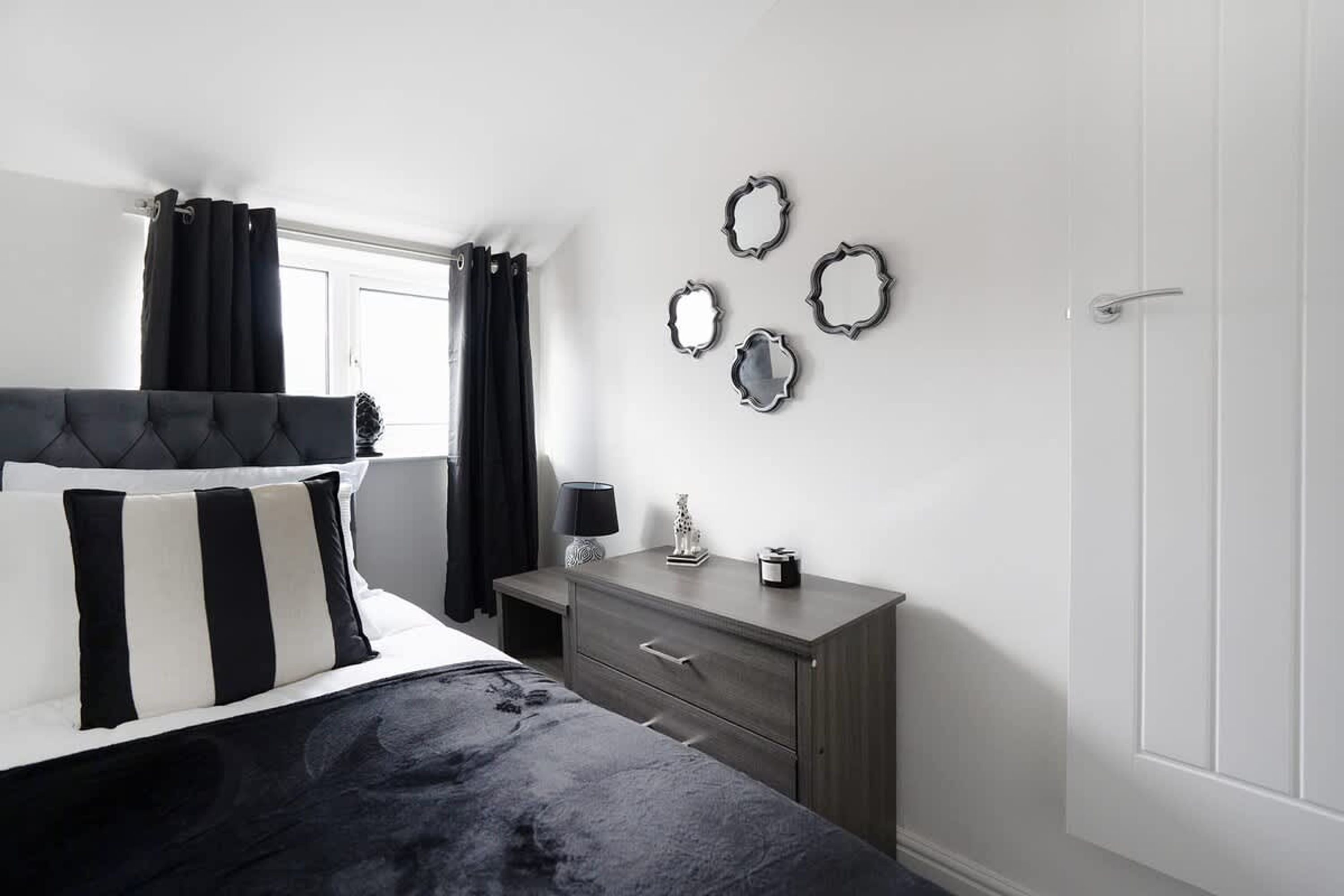 A bedroom with a bed, a dresser, a nightstand, and a door.