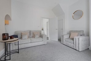 A minimalist living room with a grey sofa, a small side table, and a chair. There is a white door leading to another room. - Family Coastal Three Bedroom House Parking and Wifi (Saltburn-by-the-Sea)