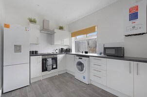 Una cocina moderna con armarios blancos, horno empotrado, lavadora y microondas.