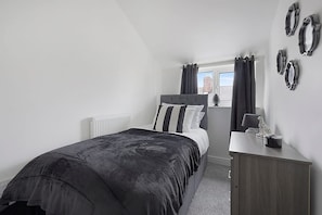 A bedroom with a bed, a bedside table, a dresser, a window with curtains, and a radiator. - Family Coastal Three Bedroom House Parking and Wifi (Saltburn-by-the-Sea)