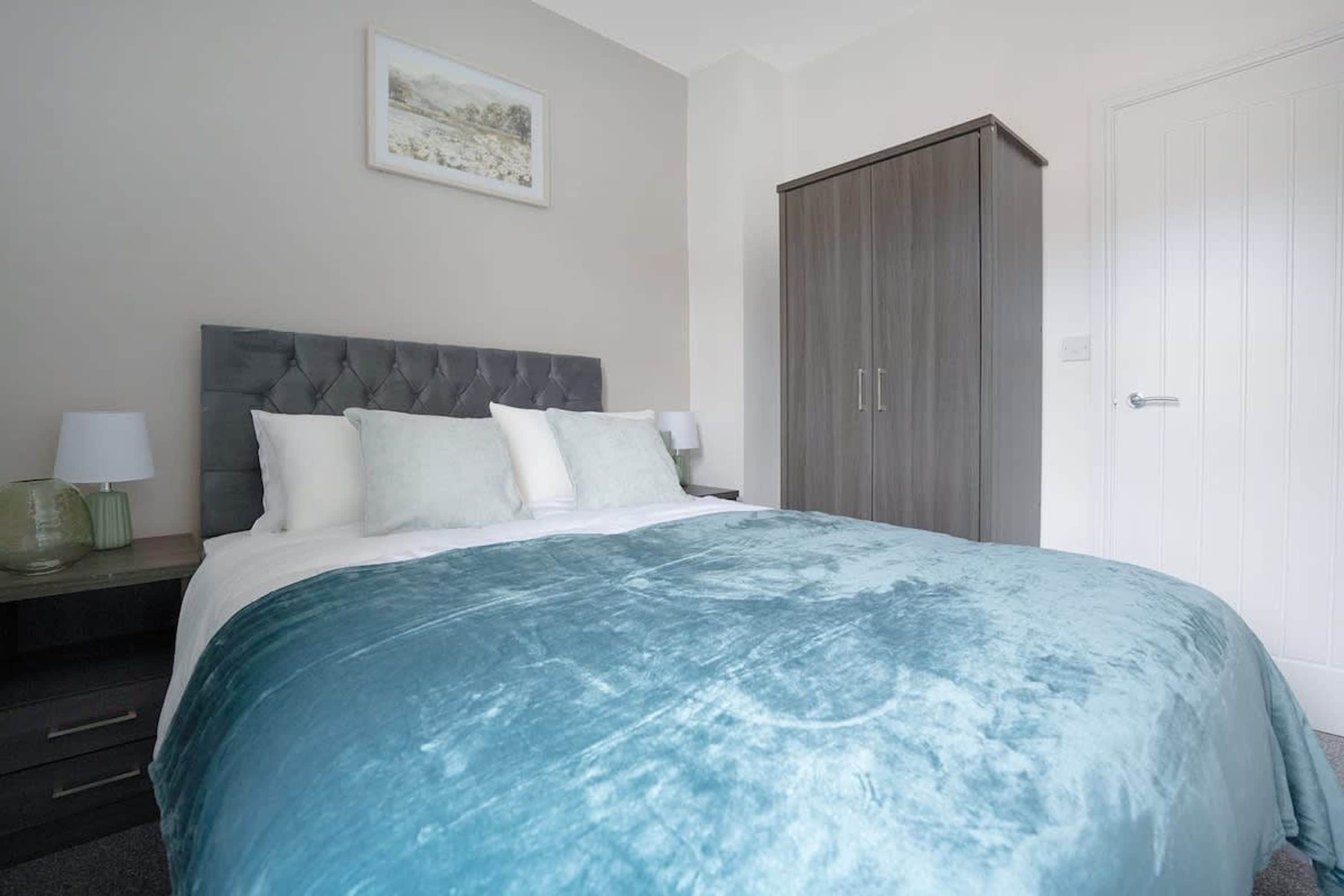 A bedroom with a large bed, a nightstand, a lamp, a wardrobe, and a door.