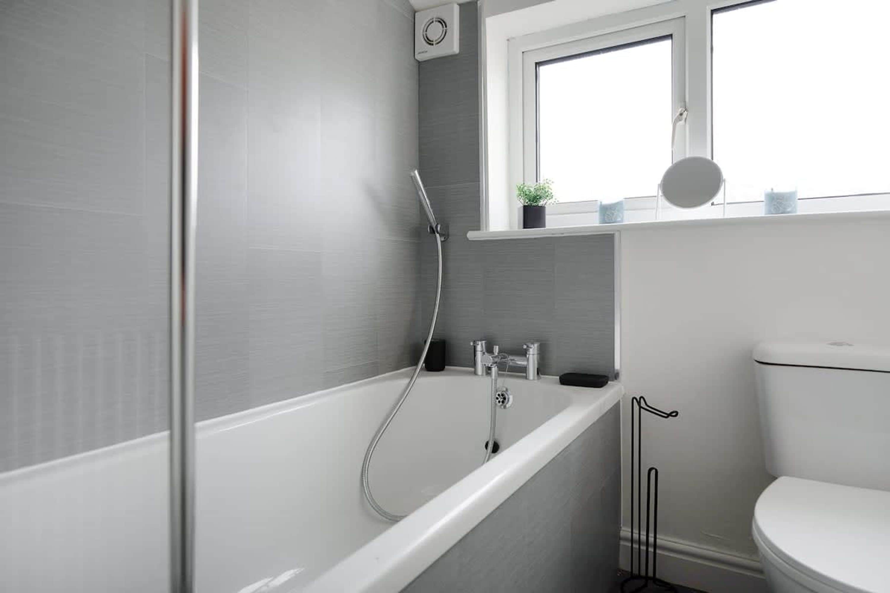 A modern bathroom with a bathtub, toilet, and a window above the sink.