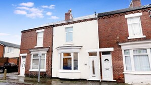 A row of terraced houses with white front doors and windows, a visible street, and a parked car. - 2BR in Dundee Free Wifi and Indoor Fireplace (Darlington)
