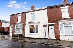 A row of terraced houses with white front doors and windows, a visible street, and a parked car. - 2BR in Dundee Free Wifi and Indoor Fireplace (Darlington)