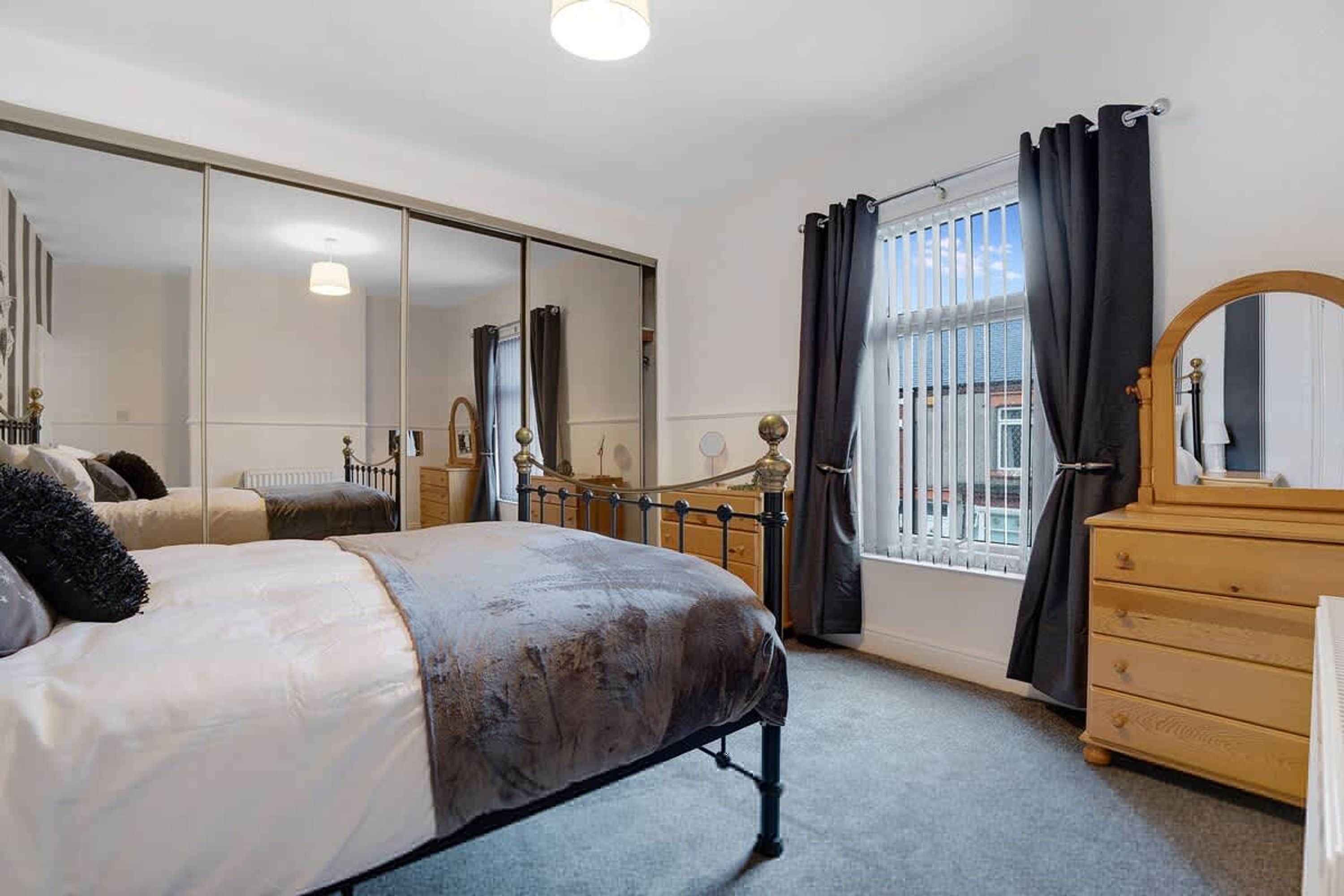Een slaapkamer met een bed, een dressoir, een spiegel en een grote kast.