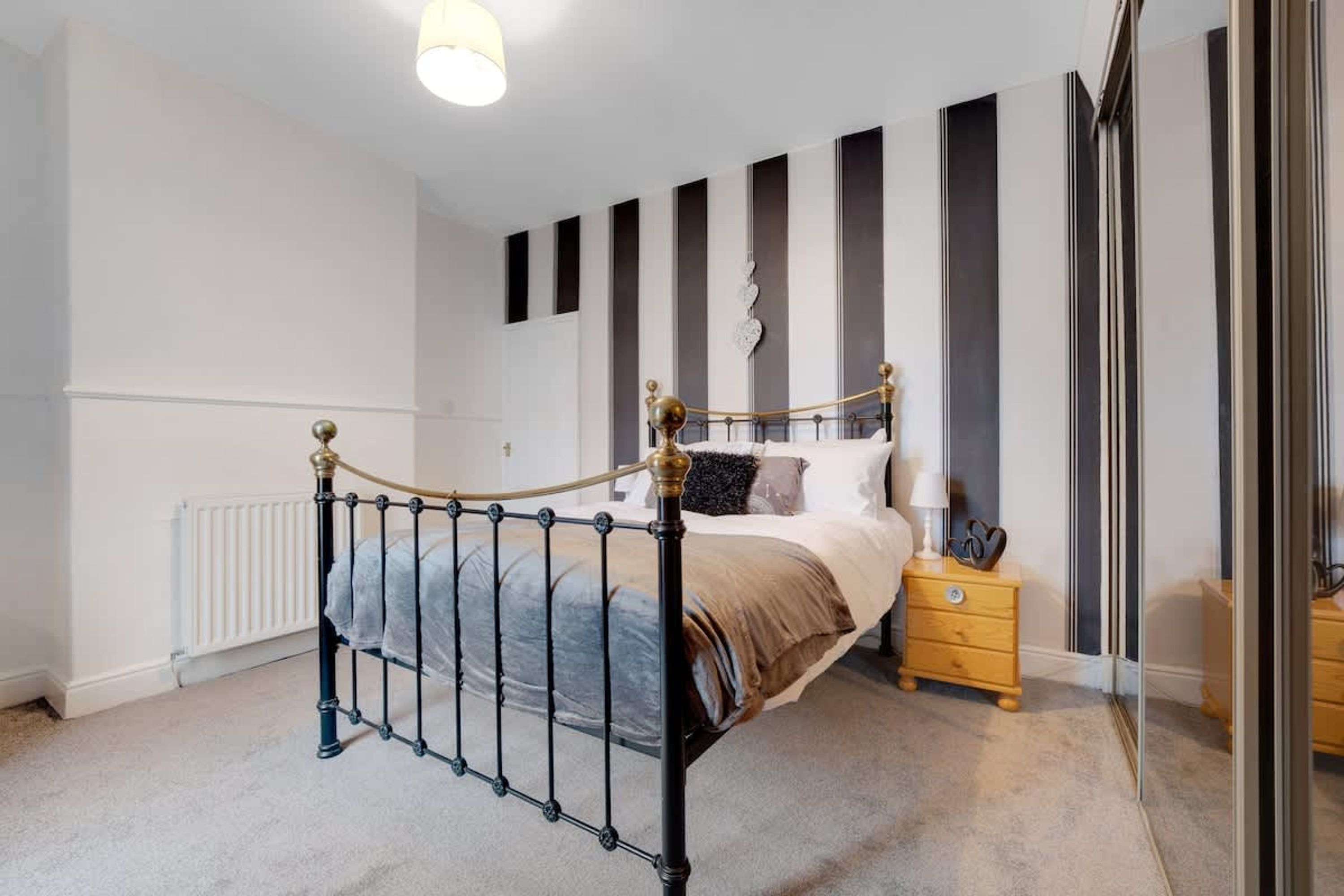 A bedroom with a metal-framed bed, a bedside table, a nightstand, and a radiator.