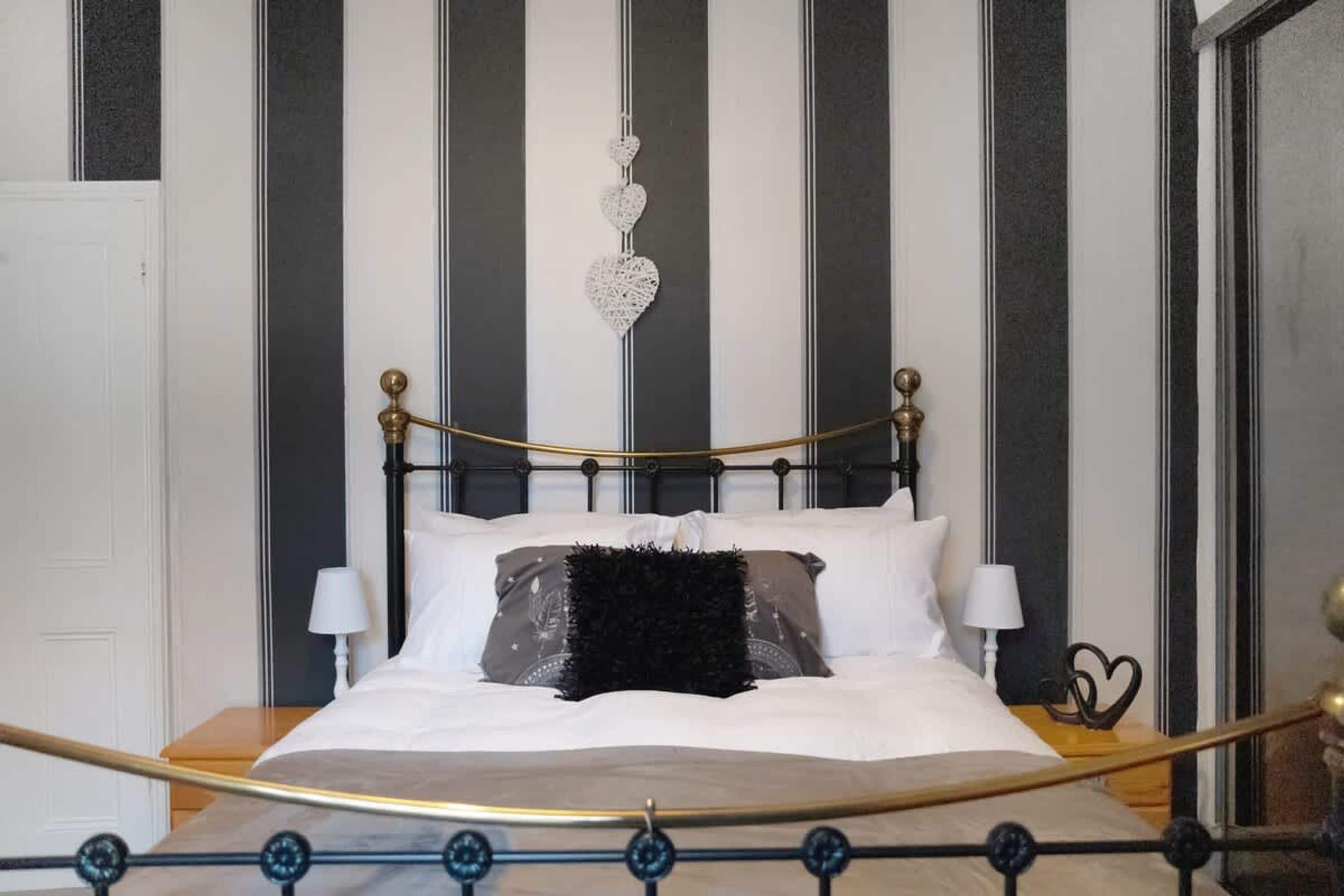 A bed with a black and gold headboard, two bedside lamps, and a decorative heart hanging from the ceiling.