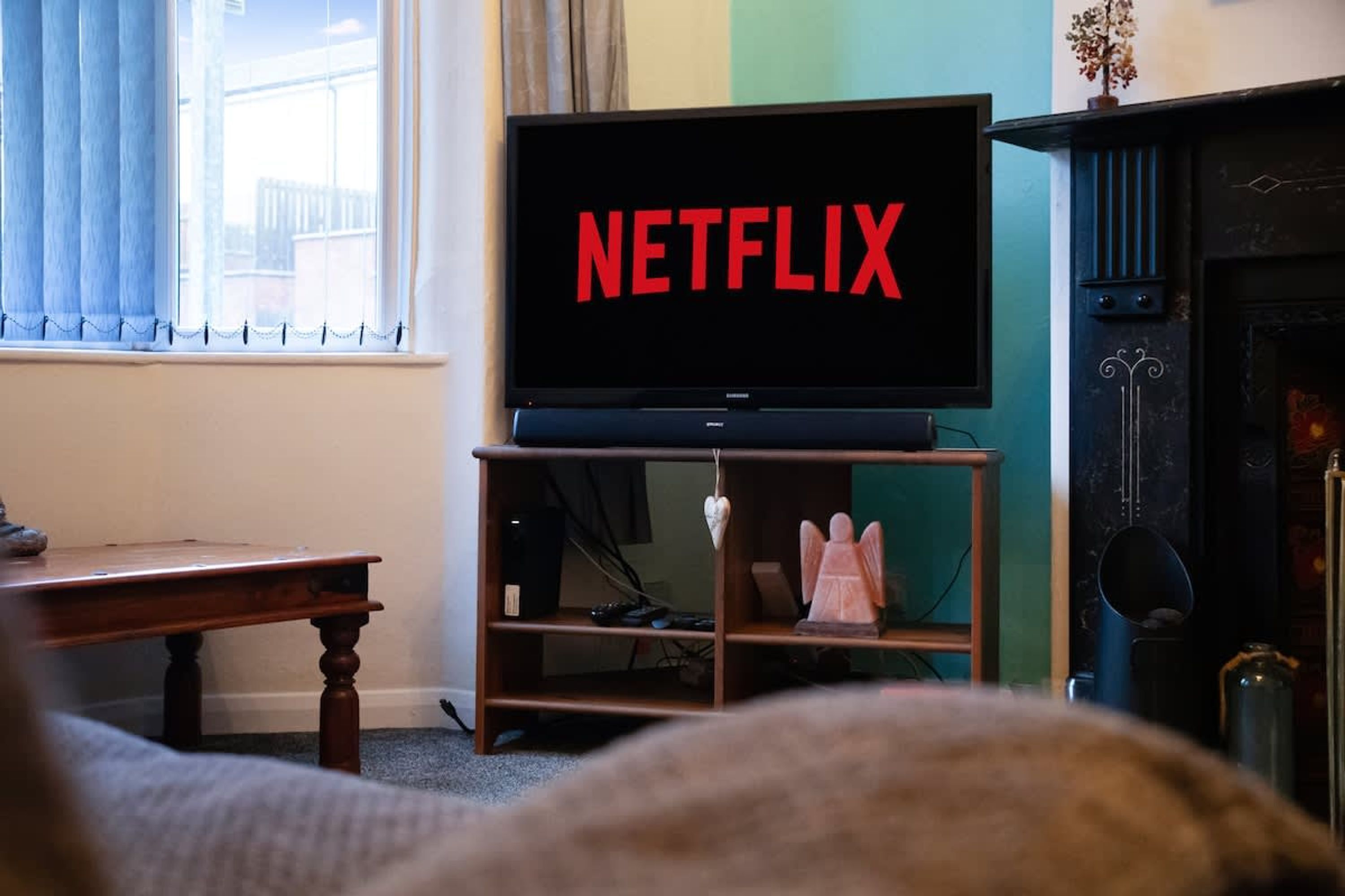 A living room with a television displaying 'NETFLIX' in red letters, a fireplace, and a window with curtains.