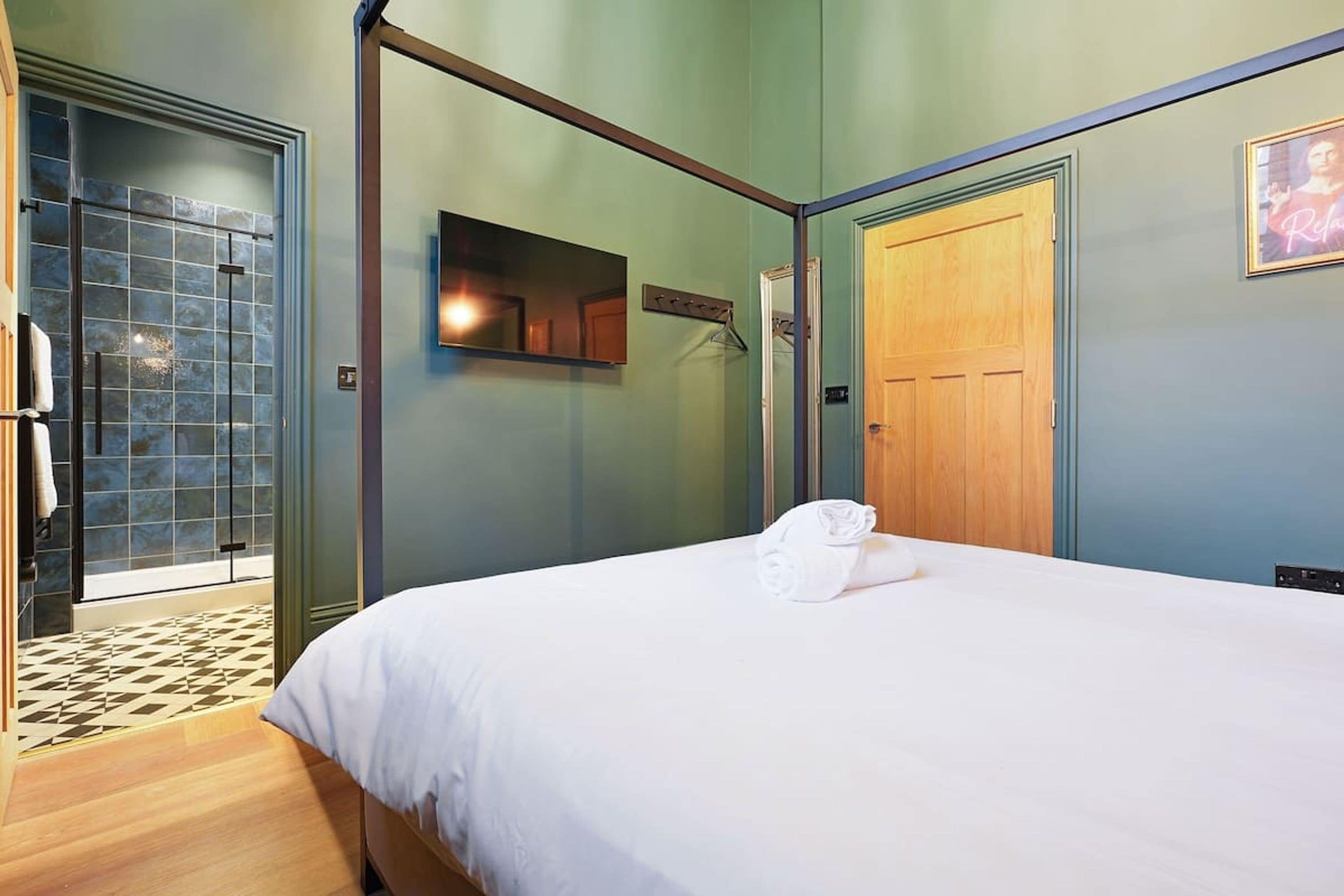 A hotel room with a bed, a wooden door, a mirror, and a tiled shower area.