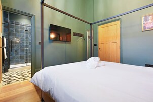 Habitación de hotel con una cama, una puerta de madera, un espejo y una zona de ducha con azulejos.