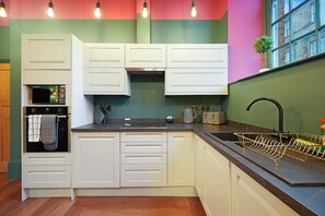 Une cuisine avec des meubles blancs, une cuisinière, un évier et une fenêtre agrémentée d’une plante.