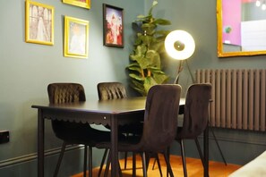 Un comedor con una mesa, sillas, una planta y cuadros en la pared.
