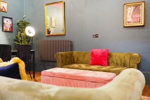 Una habitación con un sofá, una silla, una lámpara de pie, un radiador y cuadros en la pared.