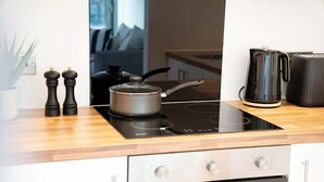 Eine moderne Küche mit einer schwarzen Induktionskochplatte, einem Herd, einem Wasserkocher und einem Toaster. Auf der Arbeitsfläche befinden sich zwei Pfeffermühlen und ein Messerblock.