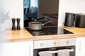 A modern kitchen with a black induction cooktop, a stove, a kettle, and a toaster. There are two pepper mills and a knife block on the countertop. - New 2BR in Media City Free Wifi (Salford)