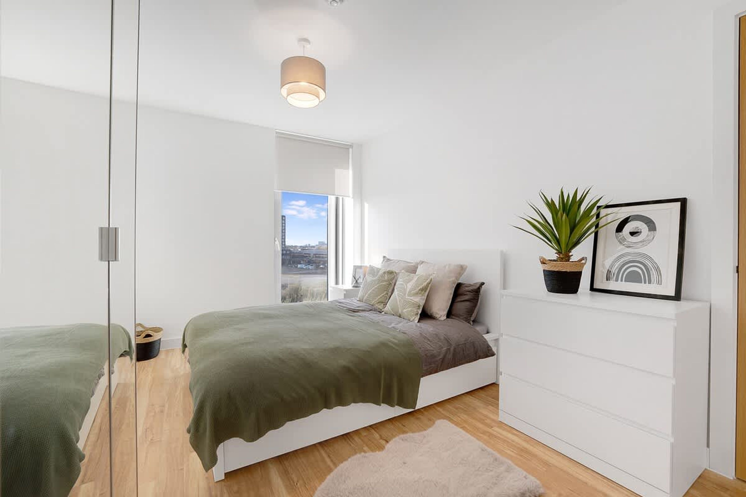 A modern bedroom with a bed, a potted plant, and a framed picture on the wall.