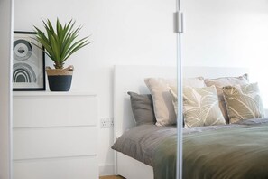 Makuuhuone, jossa on sänky, tyynyjä, kasvi ja taideteos hyllyllä.