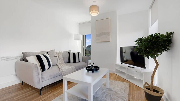 Ein modernes Wohnzimmer mit einem grauen Sofa, einem weißen Couchtisch und einem großen Fernseher auf einer weißen Ablagefläche.
