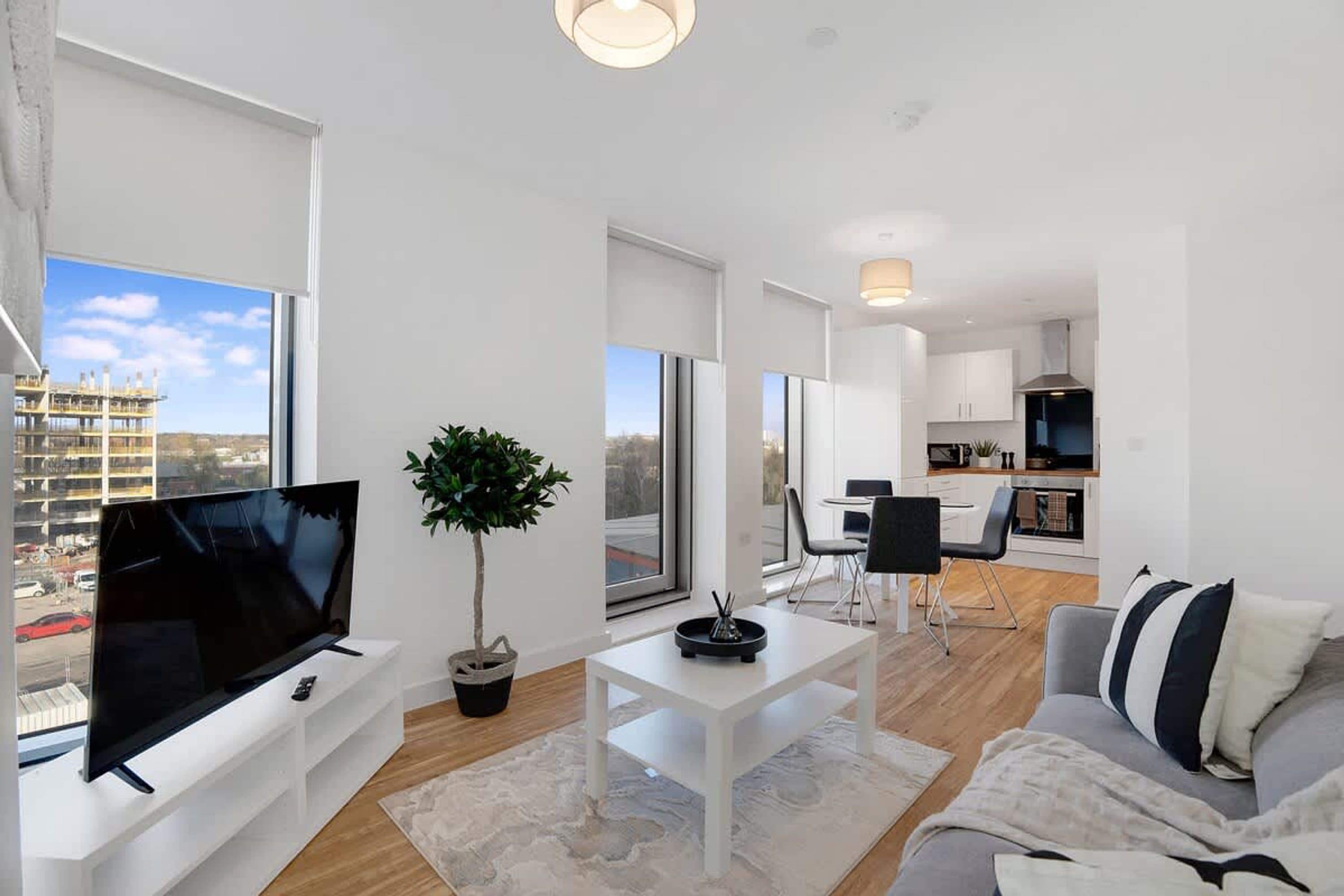 A modern living room with a flat-screen TV, a potted plant, a coffee table, and a sofa.
