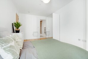 A minimalist bedroom with a bed, a small bedside table, a potted plant, and a view of a bathroom. - New 2BR in Media City Free Wifi (Salford)