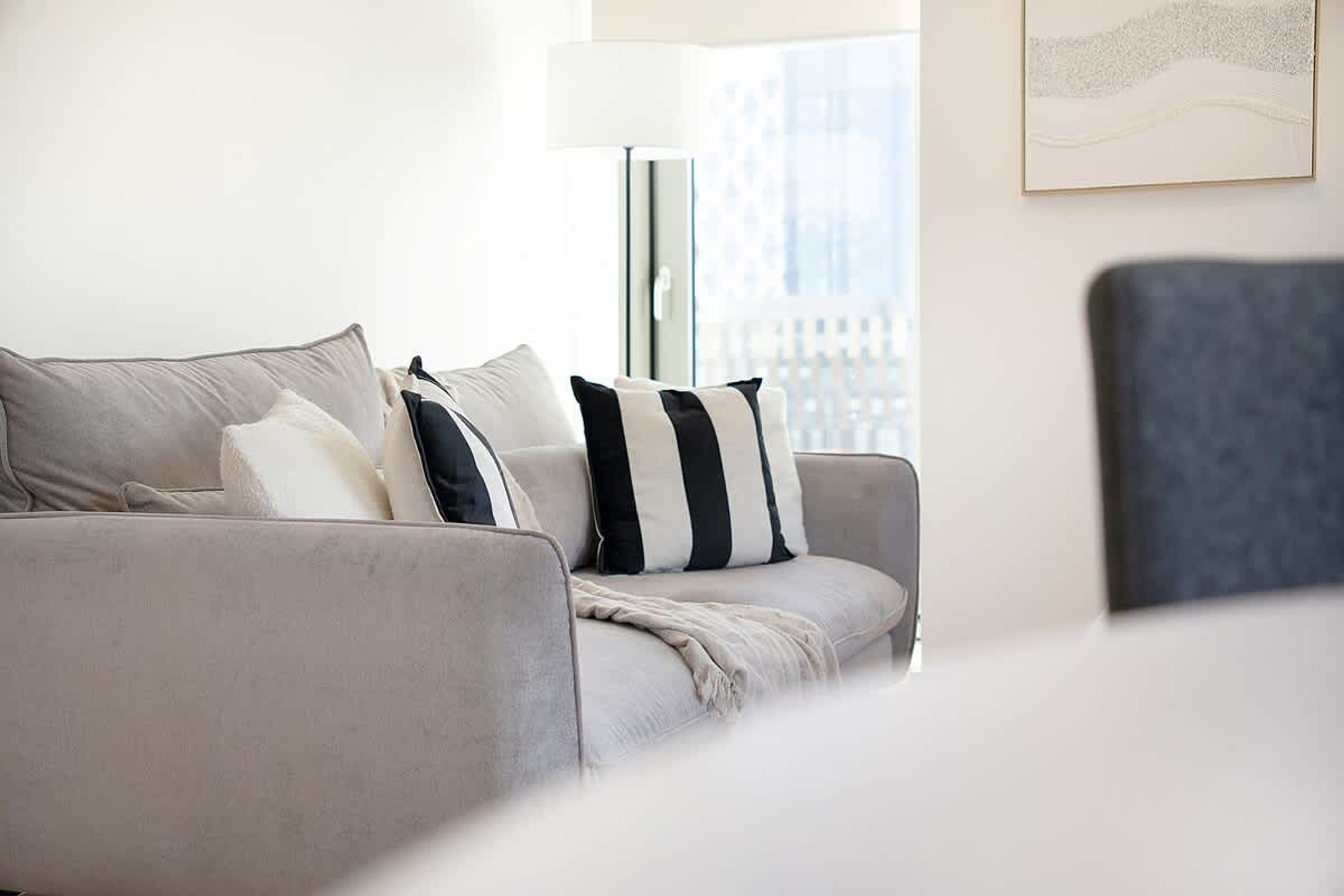 En moderne stue med en grå sofa, en gulvlampe og udsigt over byen fra vinduet.