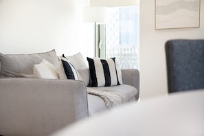 A modern living room with a grey sofa, a floor lamp, and a city view through the window. - New 2BR in Media City Free Wifi (Salford)