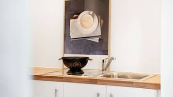 A kitchen with a wooden countertop, a black colander, a stainless steel sink, and a framed picture above the colander.
