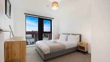 Ein modernes Schlafzimmer mit einem großen Bett, einem Nachttisch, einer Lampe und Blick zum Himmel durch ein Fenster.