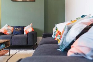 Sala de estar con un sofá, una silla y una mesa de centro. Se observa una estantería de pared con algunos objetos.