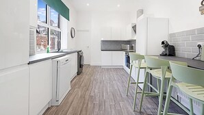 A modern kitchen with white cabinetry, a built-in dishwasher, and a window with a view of the outside. - Spacious Five Bedroom Family Home Group Stay Wifi (Sunderland)
