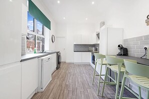 A modern kitchen with white cabinetry, a built-in dishwasher, and a window with a view of the outside. - Spacious Five Bedroom Family Home Group Stay Wifi (Sunderland)